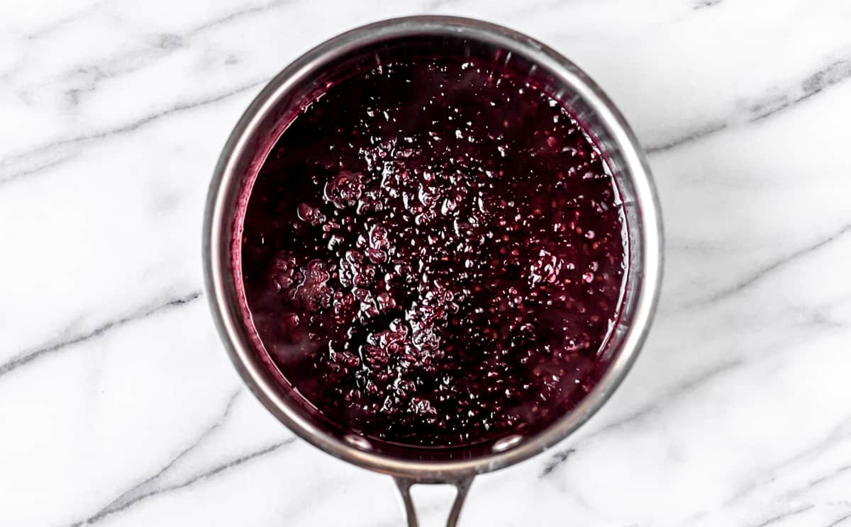 Blackberry sauce in a pot on a marble background.