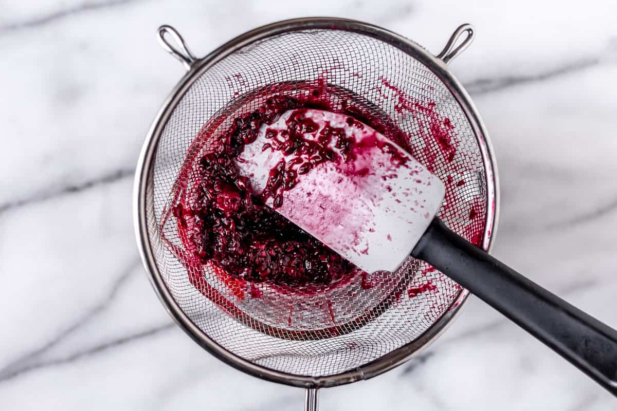 Blackberries being pressed through a sieve with a spatula.