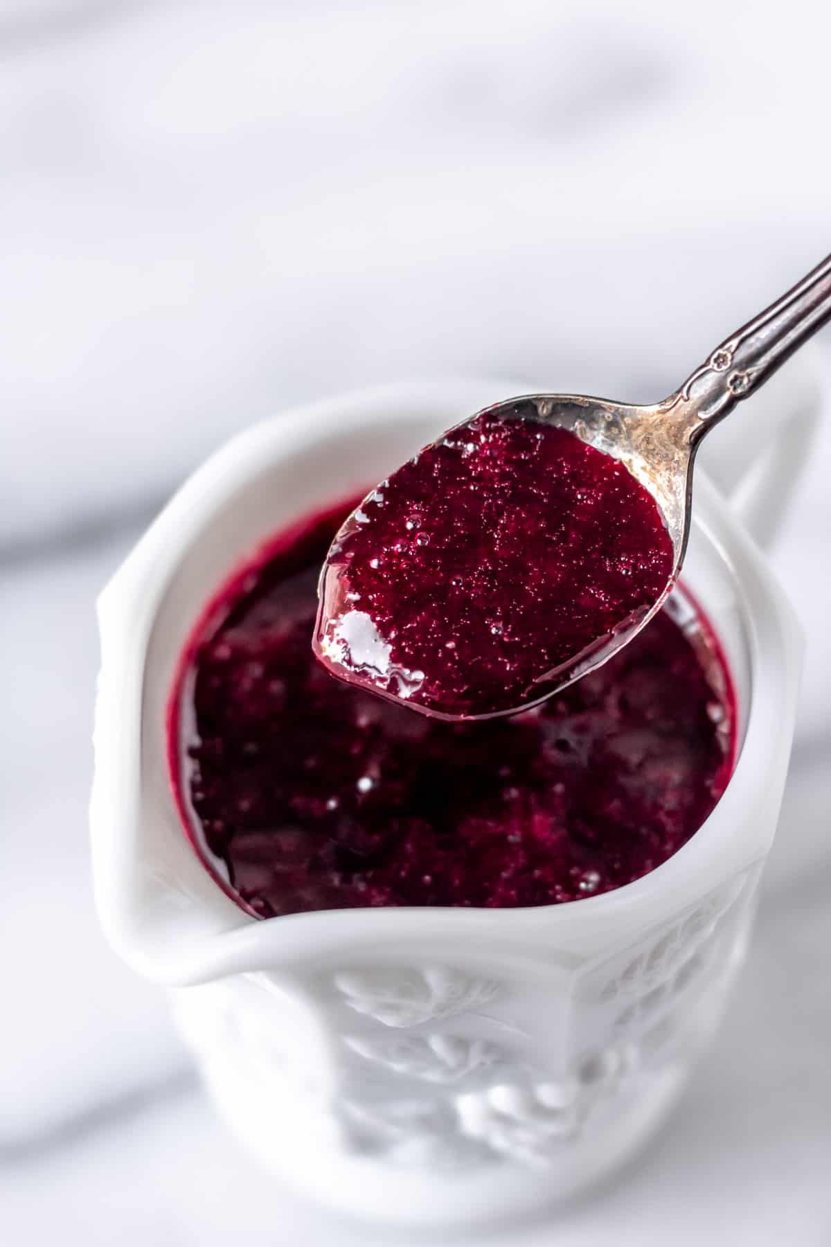 A spoonful of blackberry syrup being lifted up over a jar.