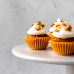 A mini carrot cake cupcake on a cake stand with a gray background.