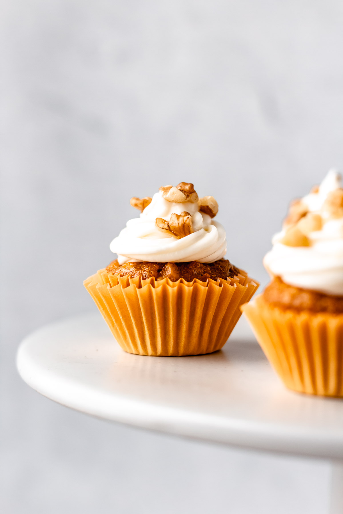 A mini carrot cake cupcake on a cake stand with a gray background.