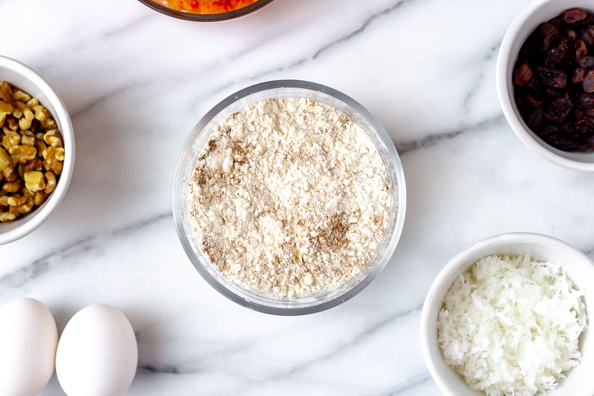 Dry ingredients for carrot cake in a small bowl with other ingredients around it.