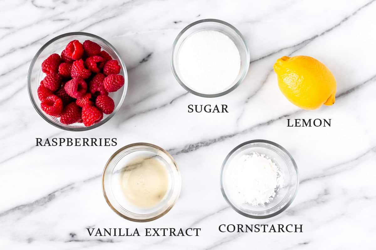 Ingredients to make raspberry sauce on a marble background with labels.