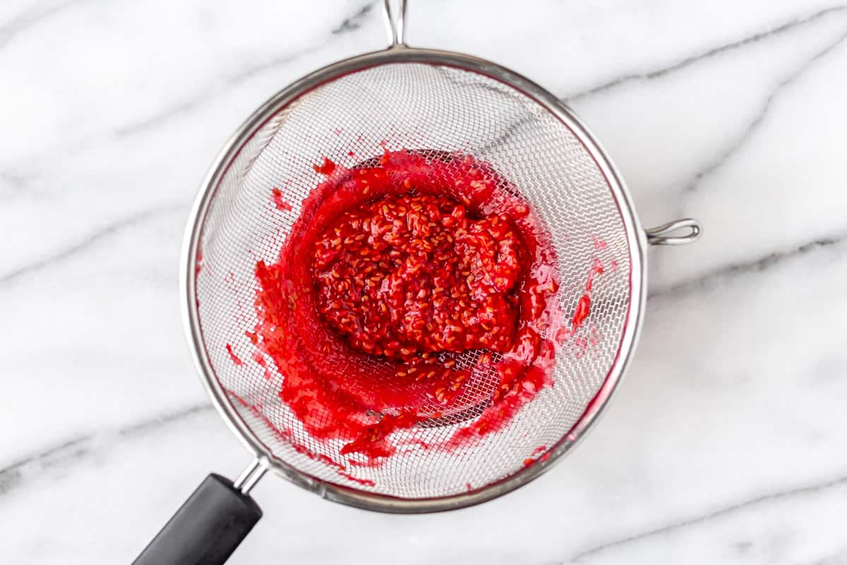 Straining raspberry sauce through a sieve so only seeds remain.