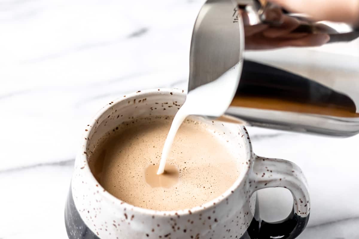 Frothed milk being poured into a mug of coffee.
