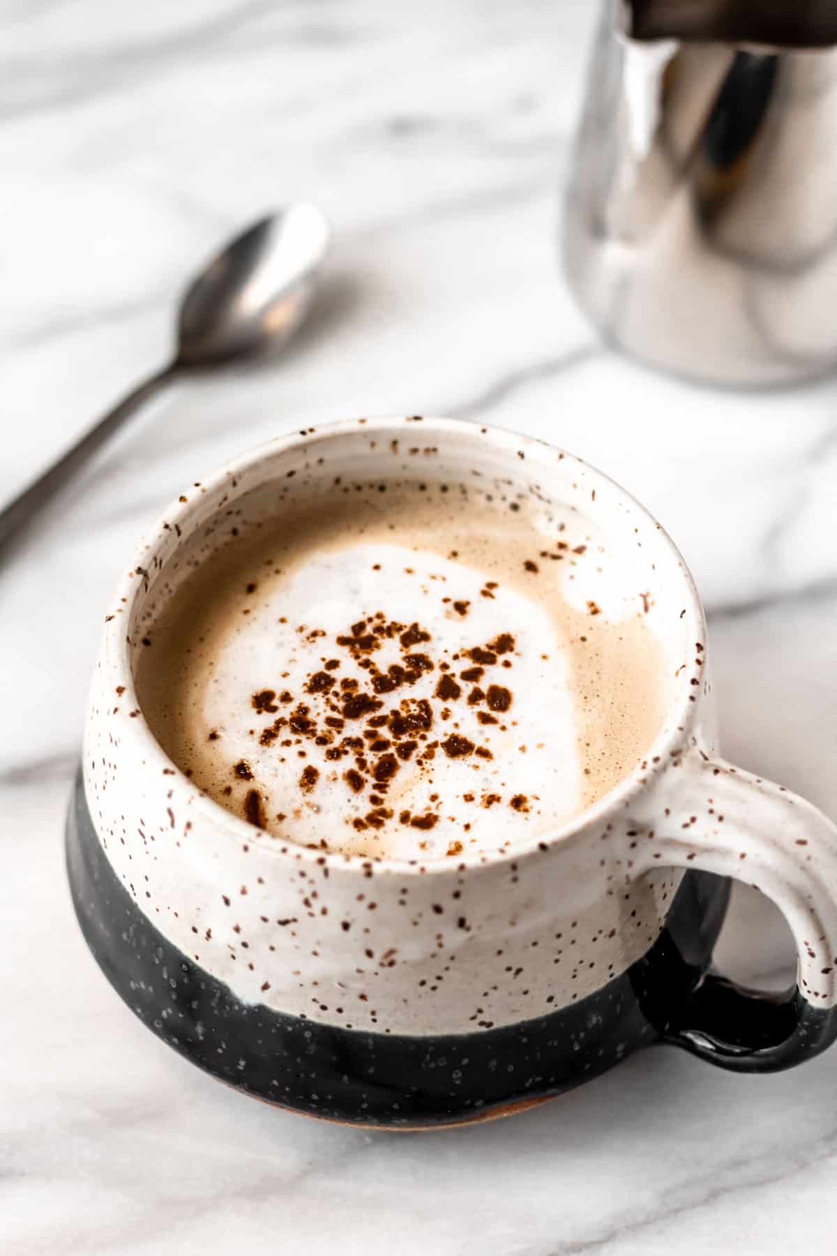 A Baileys Salted Caramel Mocha Latte in a mug with a spoon and steaming pitcher in the background.