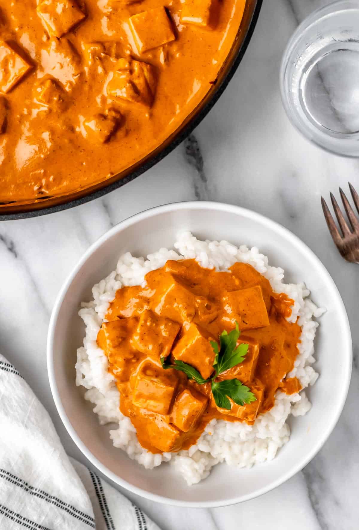 Overhead of a white bowl of rice and butter paneer with the skillet of butter paneer partially showing.