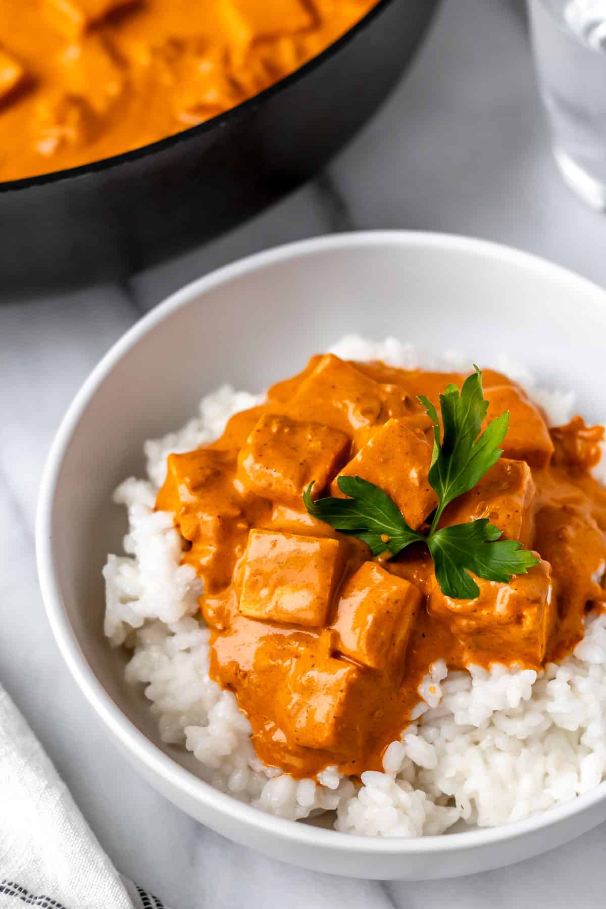 Butter paneer in a bowl with rice and part of a skillet with more butter paneer in it showing.