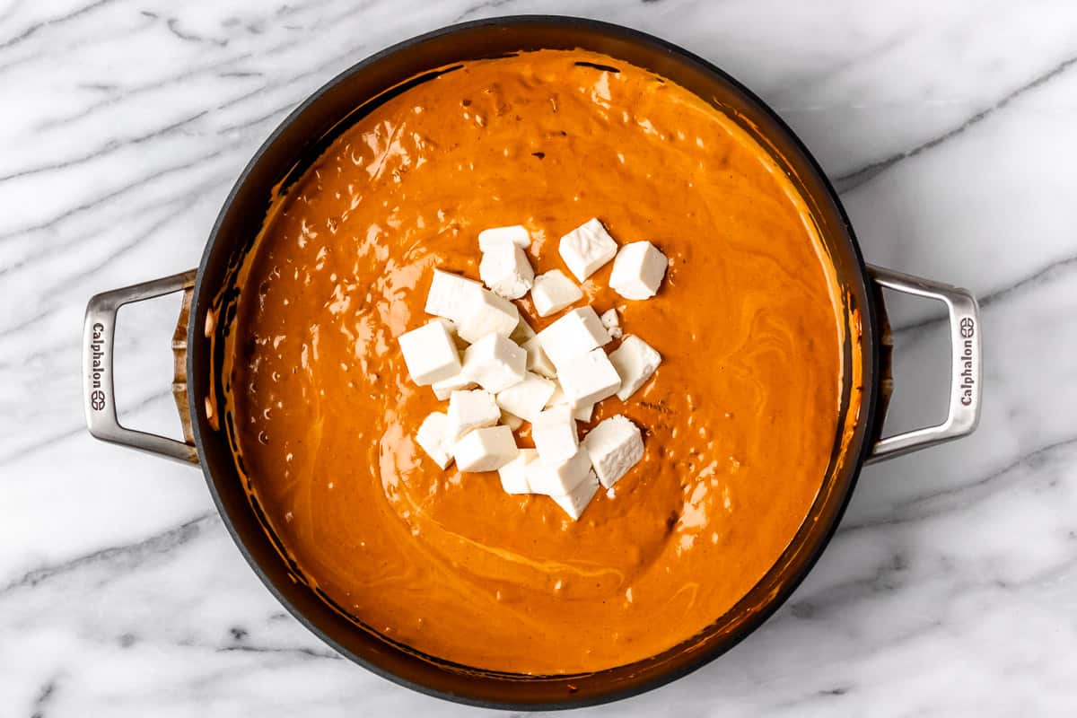 Cubes of paneer on top of butter gravy in a black skillet.