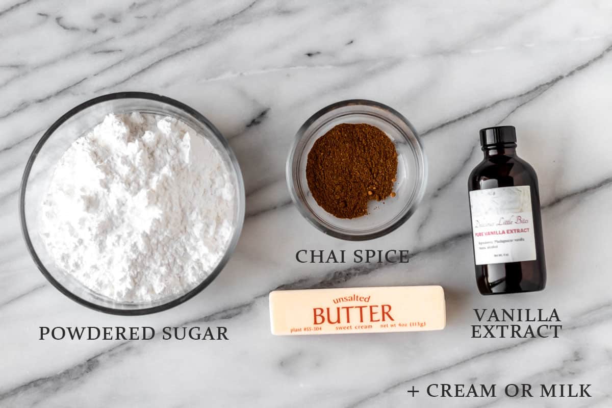 Ingredients needed to make chai buttercream frosting on a marble background with text overlay.