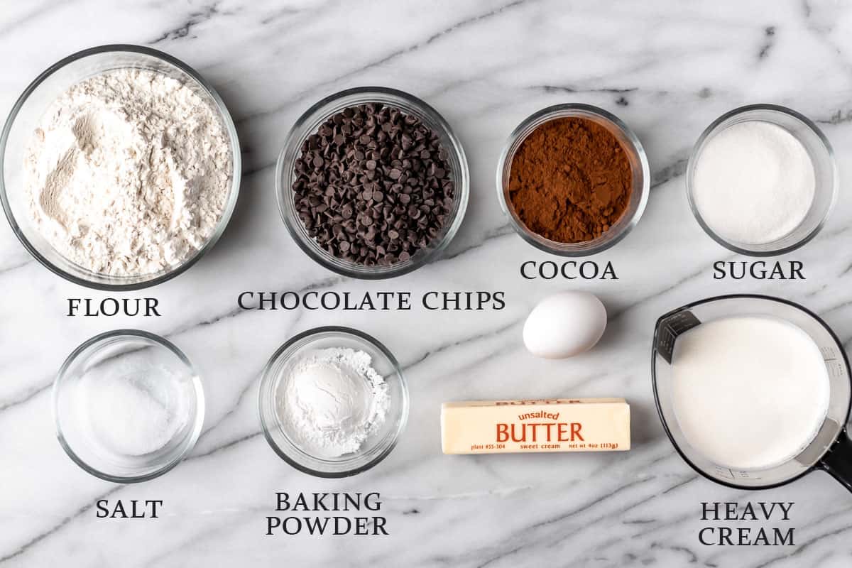Ingredients to make chocolate scones on a marble background with text overlay.