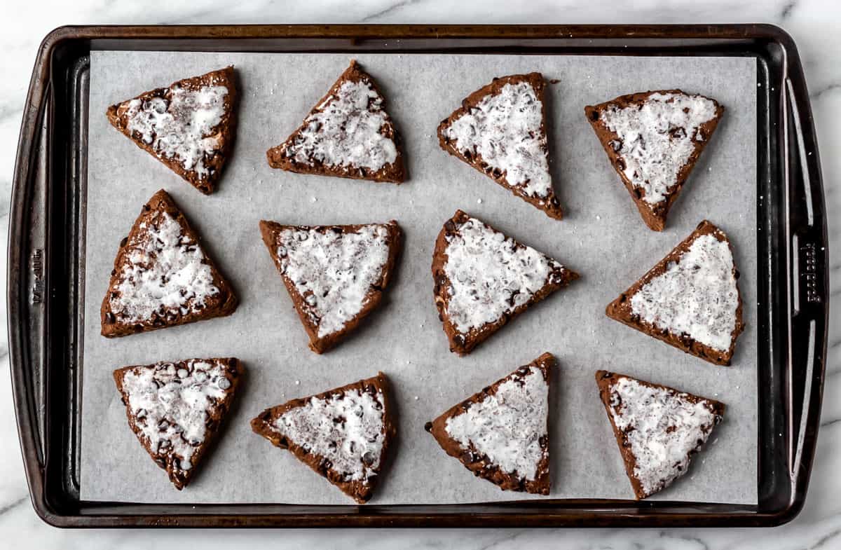 Chocolate scones cut into triangles and topped with cream prior to baking.