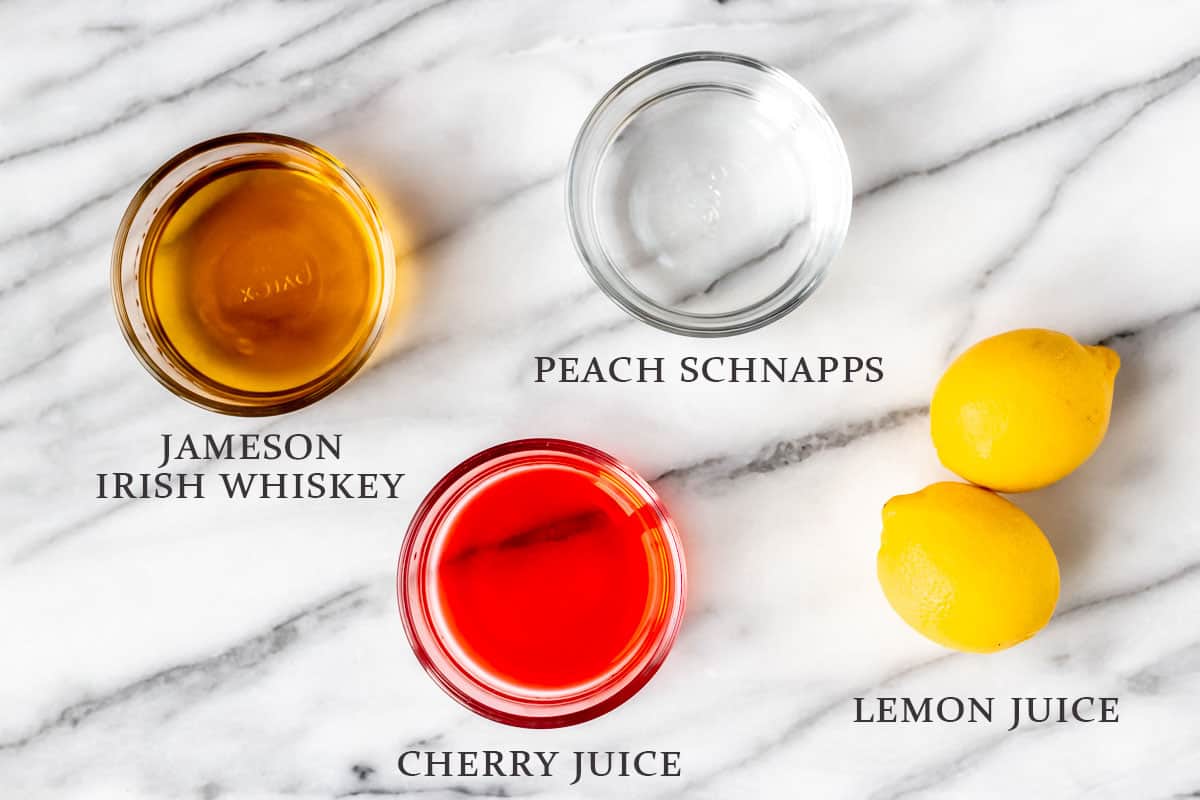 Ingredients to make an Irish Sunset cocktail on a marble background with text overlay.