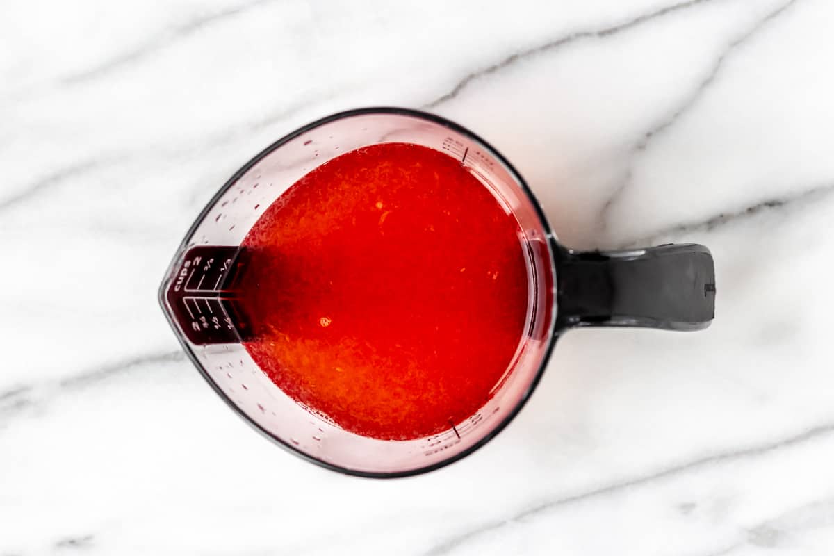 Ingredients for a cocktail in a measuring cup on a marble background.