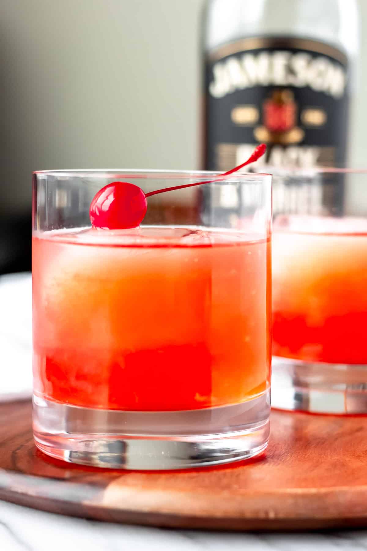 Close up of an Irish Sunset cocktail on a wood board with a bottle of Jameson Irish Whiskey in the background.