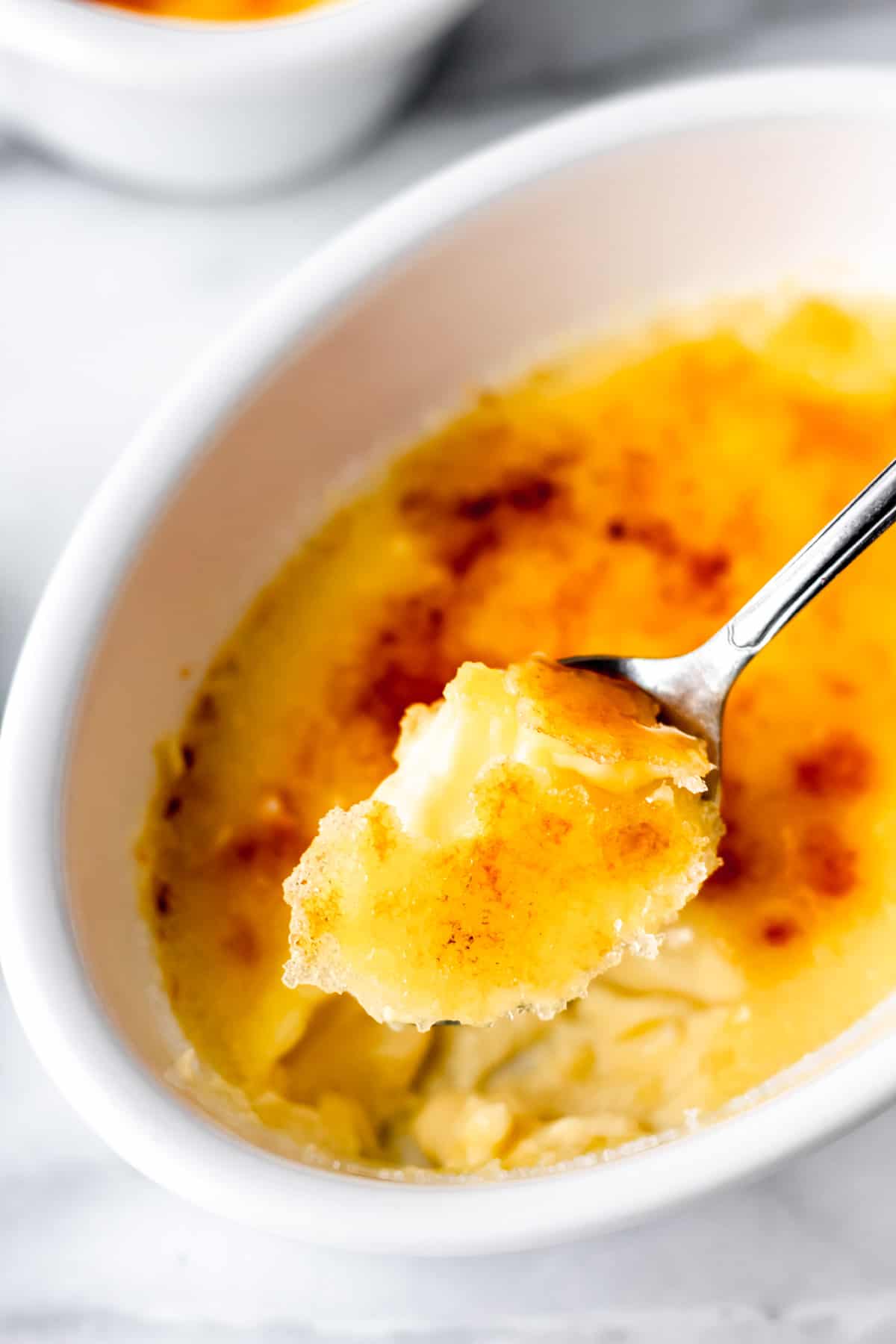 A spoonful of creme brulee being lifted up over the ramekin.