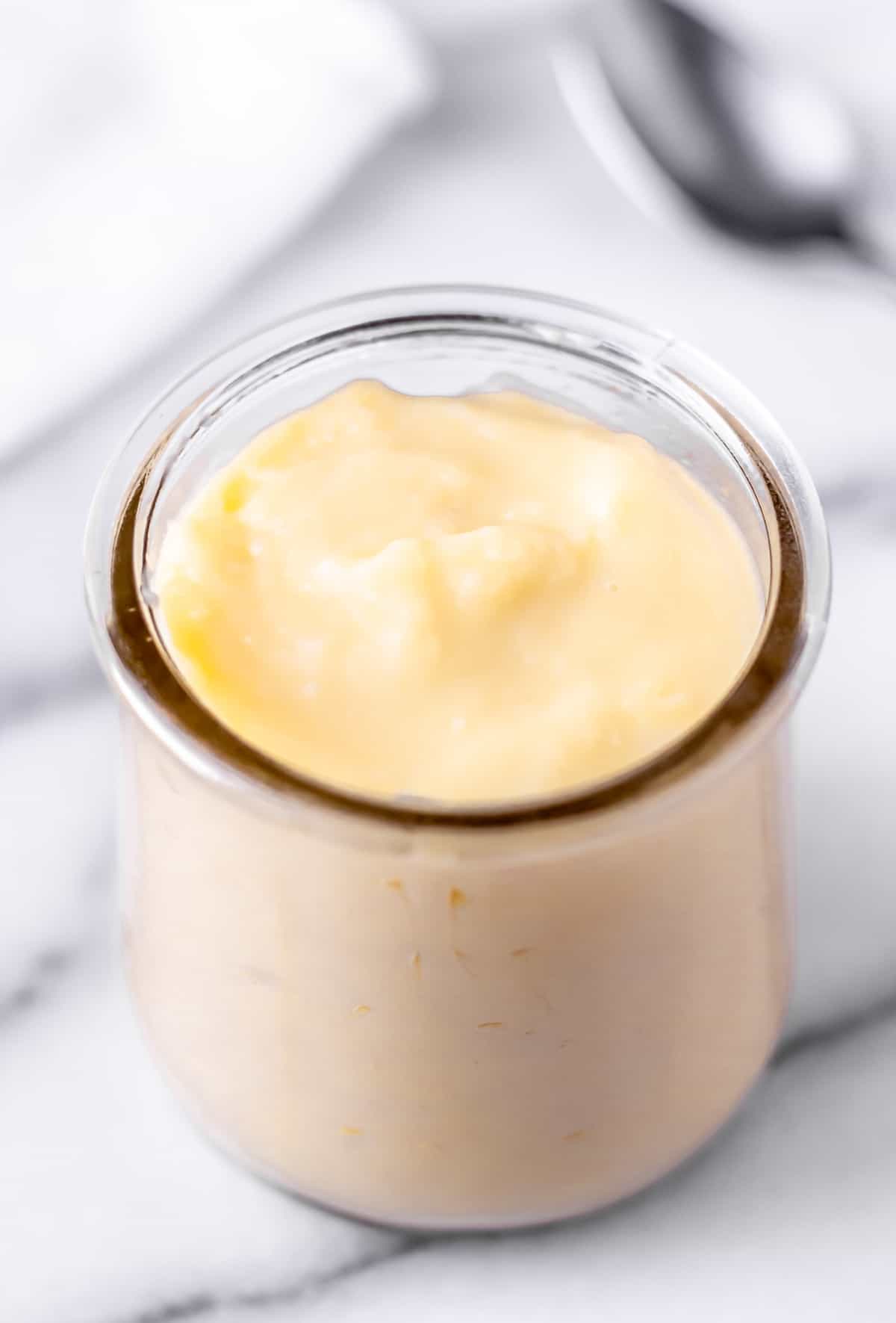 Pastry cream in a glass jar with a spoon and napkin in the background.