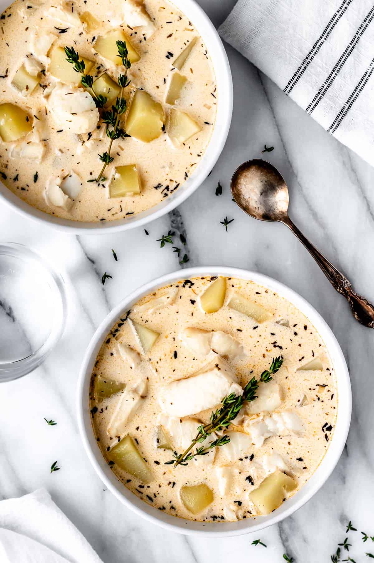 Overhead of two bowls of Cod Chowder with a spoon and kitchen towel around them.