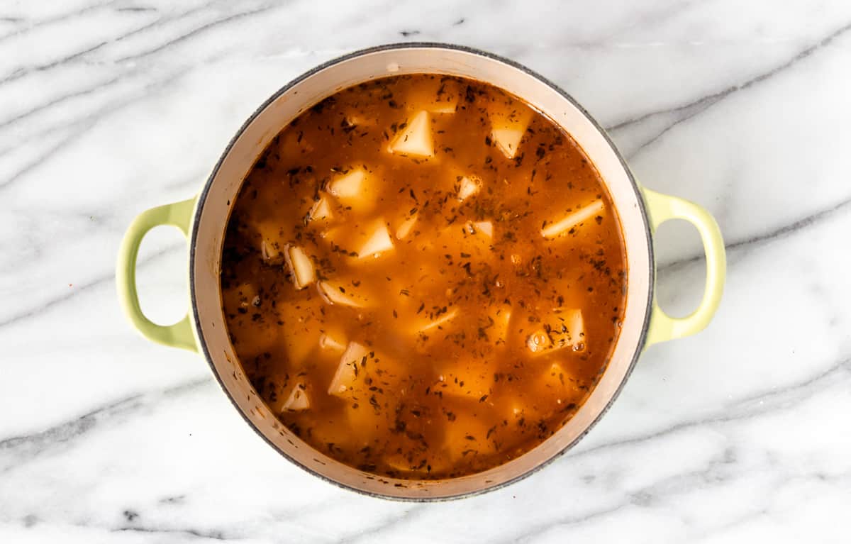 Potatoes and aromatics cooking in seafood stock in a Dutch oven.