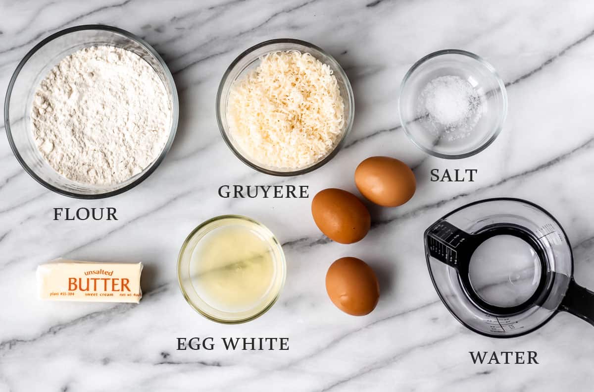 Ingredients needed to make gougeres on a marble table with text overlay.