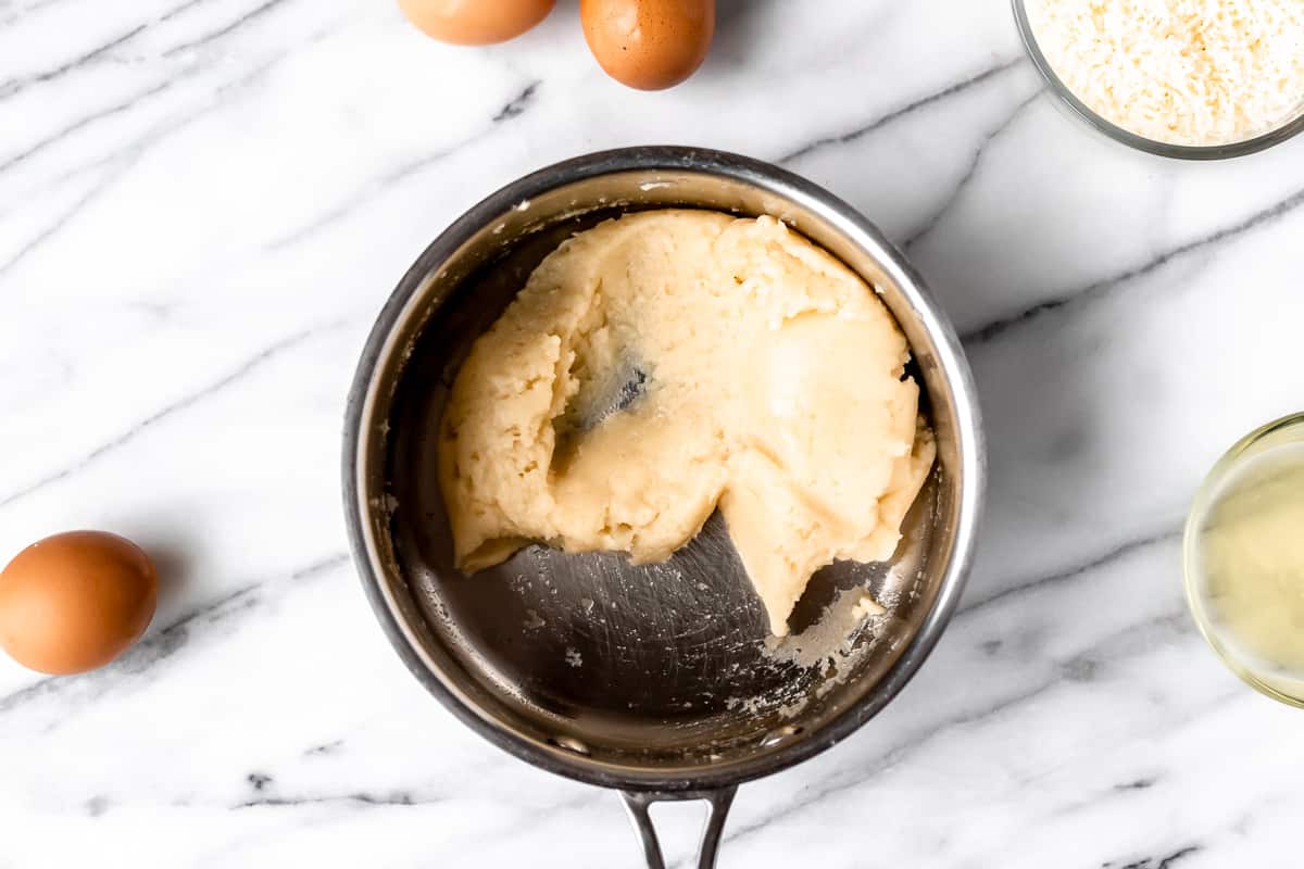 Dough in a pot on a marble table with other ingredients around it.