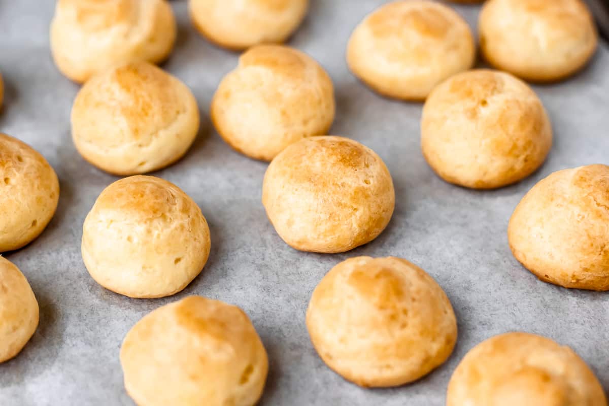 Baked gougeres on a parchment lined baking sheet.