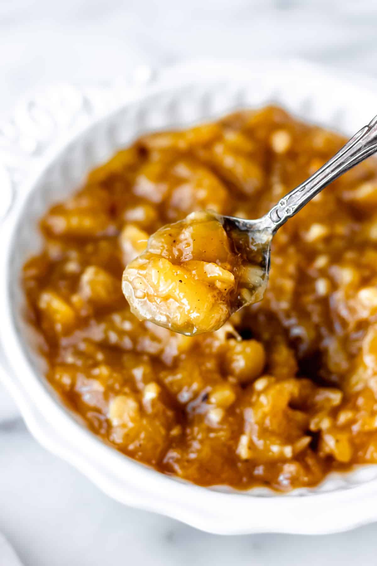 Mango chutney on a spoon being held over a bowl of more chutney.