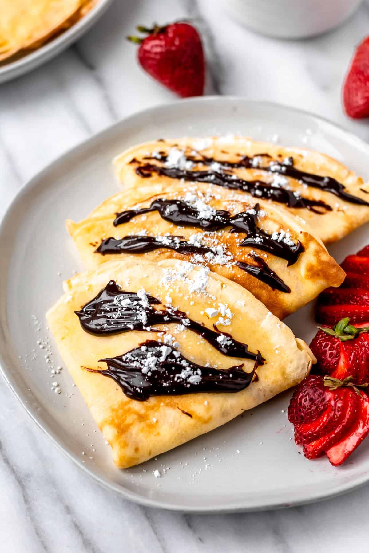 Close up of 3 sweet crepes on a plate with strawberries.