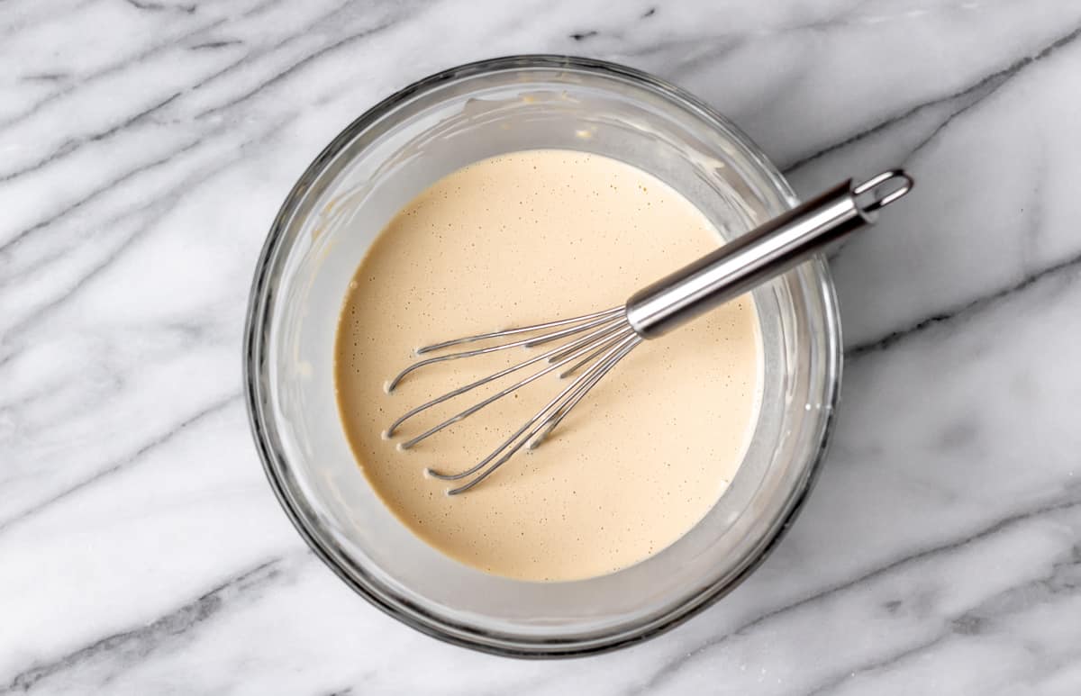 Thin crepe batter in a glass bowl with a whisk.