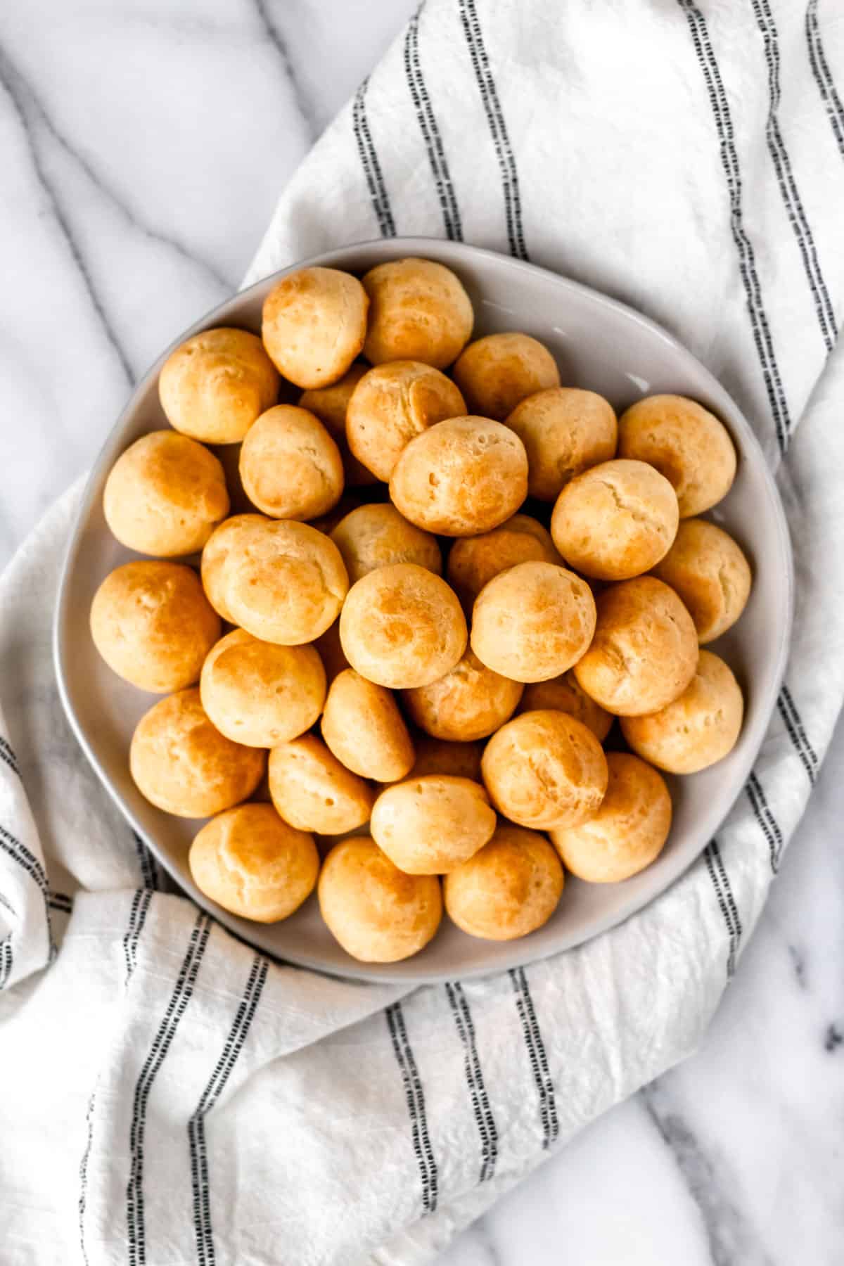 Overhead of a plate of gougeres with a stiriped kitchen towel underneath.