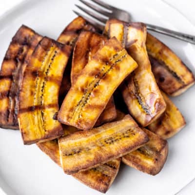 Grilled plantains on a white plate with a fork.