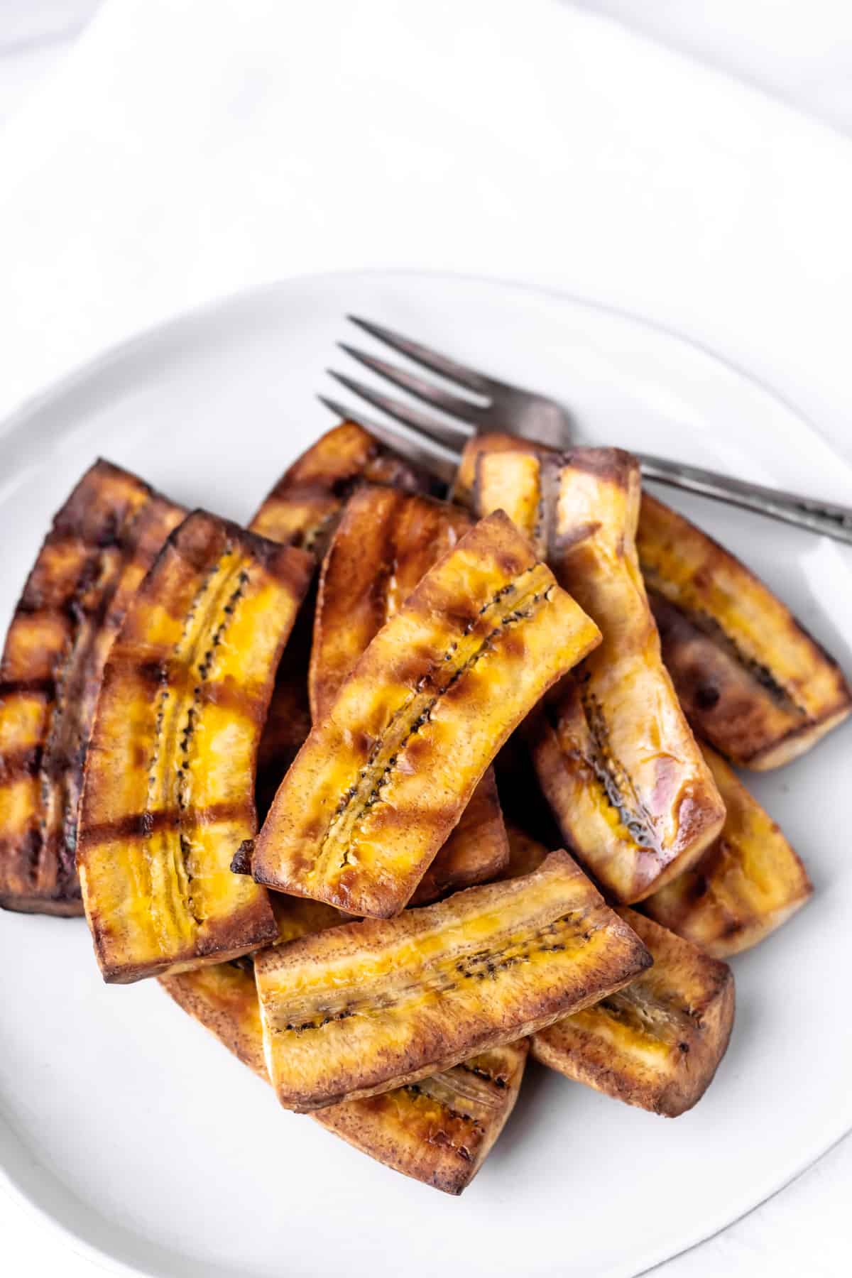 A plate of grilled plantains with a fork.