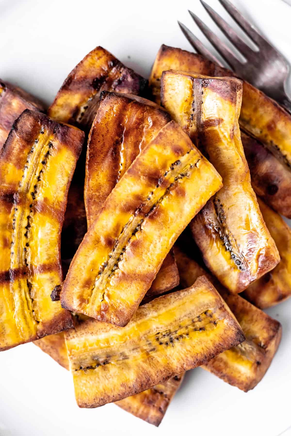 Overhead of a plate of grilled plantains with a fork on it.