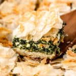 A serving of spanakopita being lifted up over the casserole dish with a server.