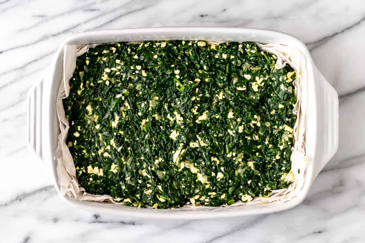 Spanakopita filling on top of sheets of phyllo dough in a rectangular casserole dish.