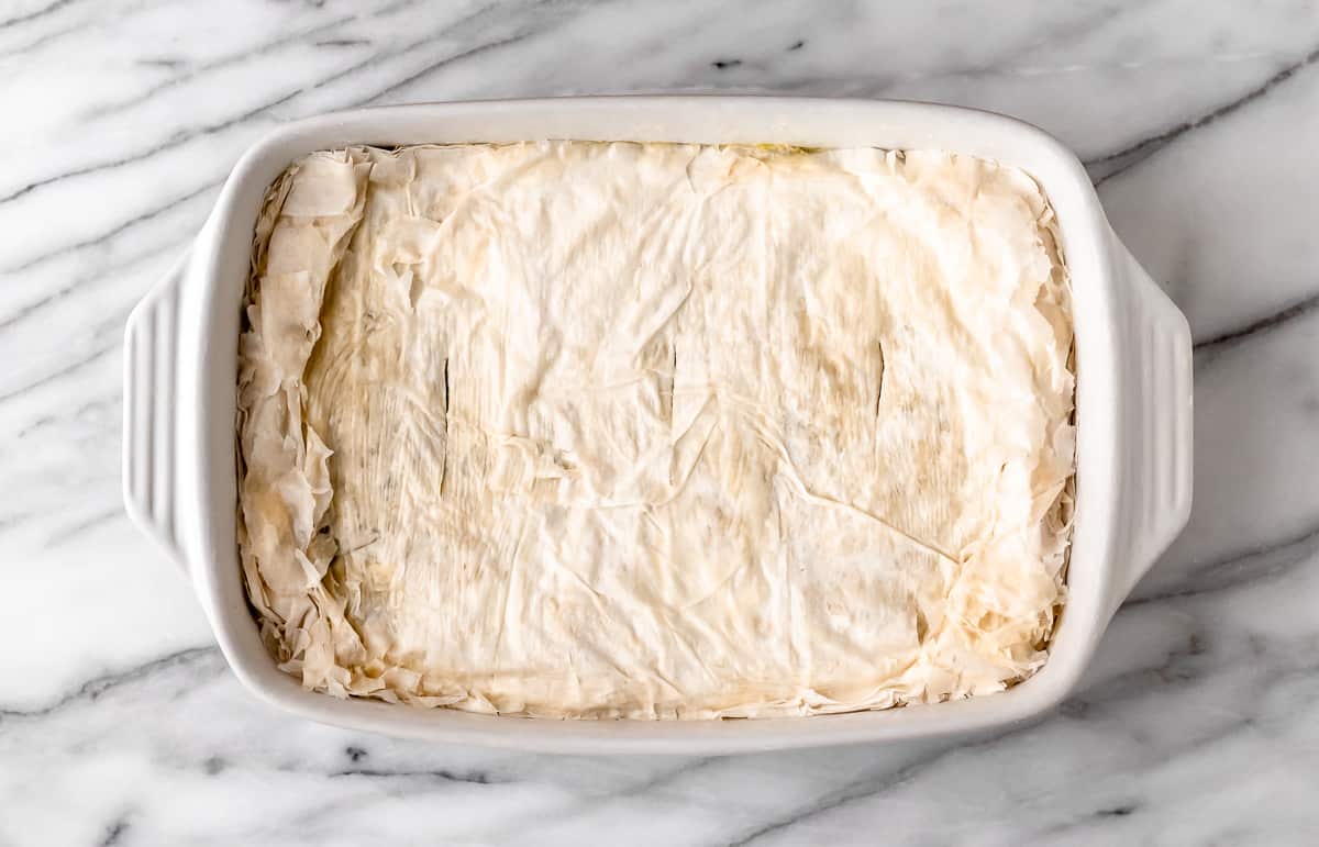 An unbaked spanakopita casserole in a rectangular casserole dish.