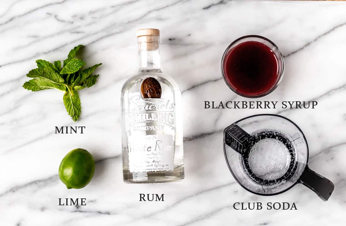 Ingredients needed to make a blackberry mojito on a marble background with text overlay.