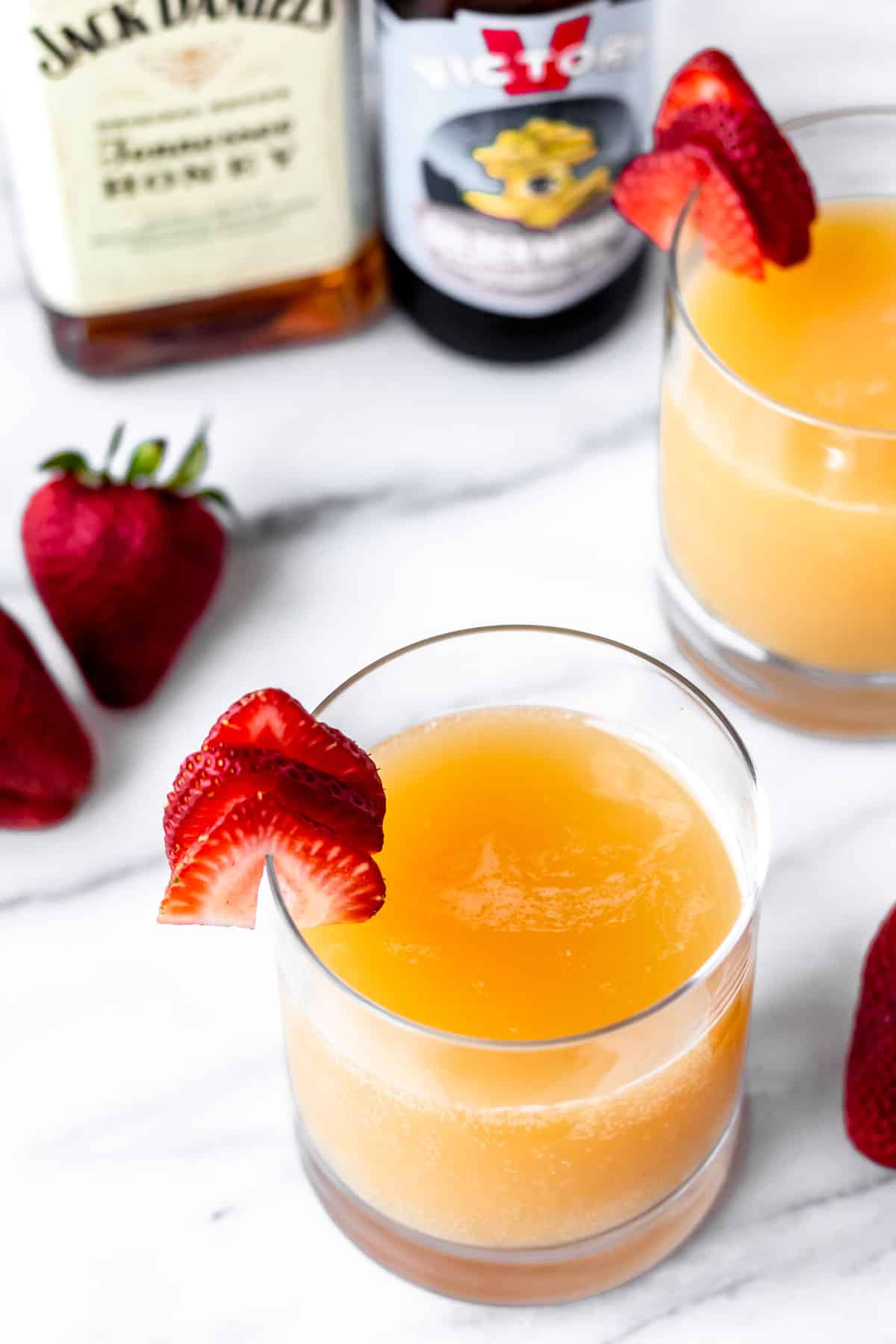 Two manmosa cocktails with strawberries and the bottles of whiskey and beer used to make them.