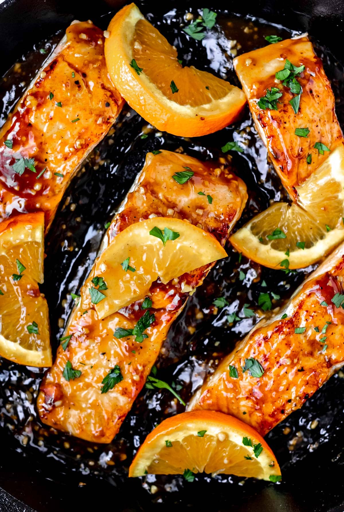 Filets of orange salmon and orange slices in a cast iron pan.