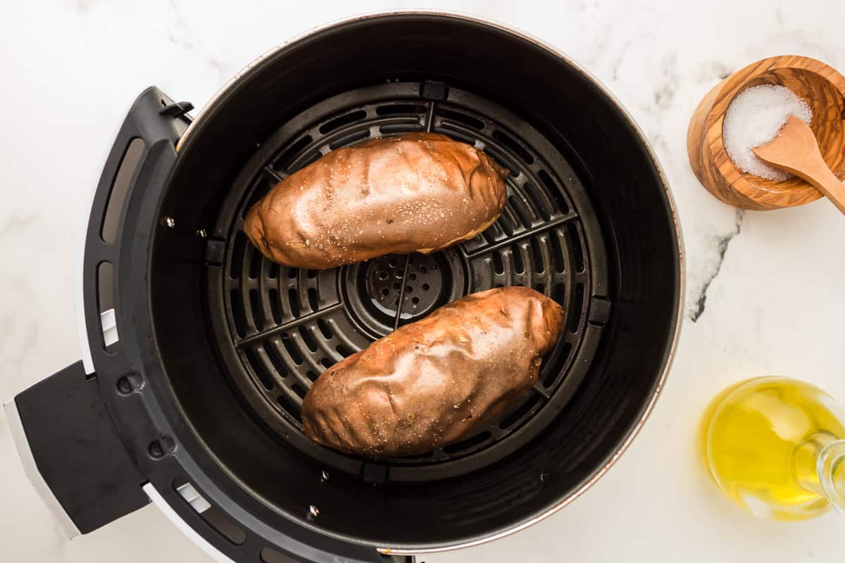 Two sweet potatoes inside the basket of an air fryer.