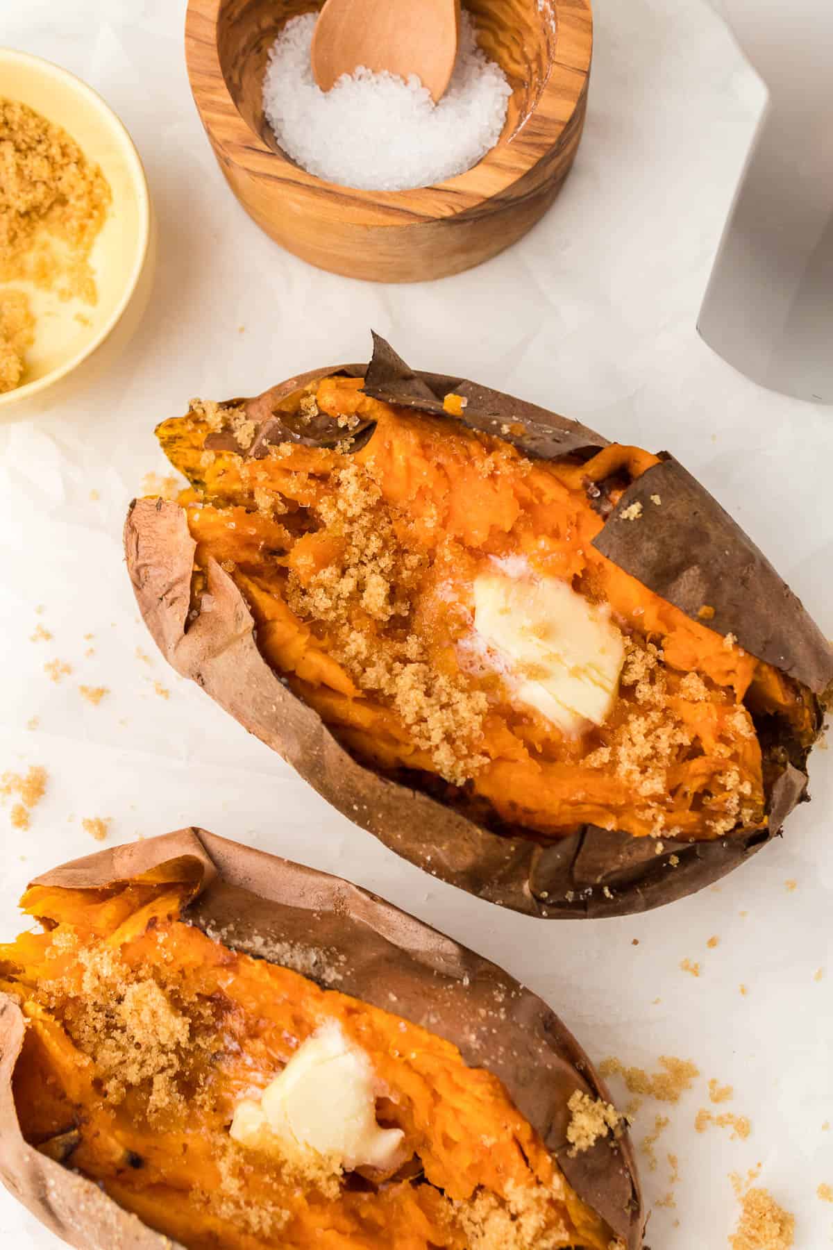 Overhead of two air fried baked sweet potatoes with butter and brown sugar on them.