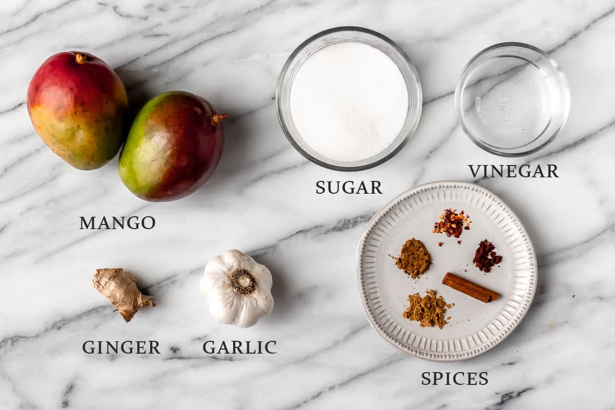 Ingredients needed to make mango chutney on a marble table with text overlay.