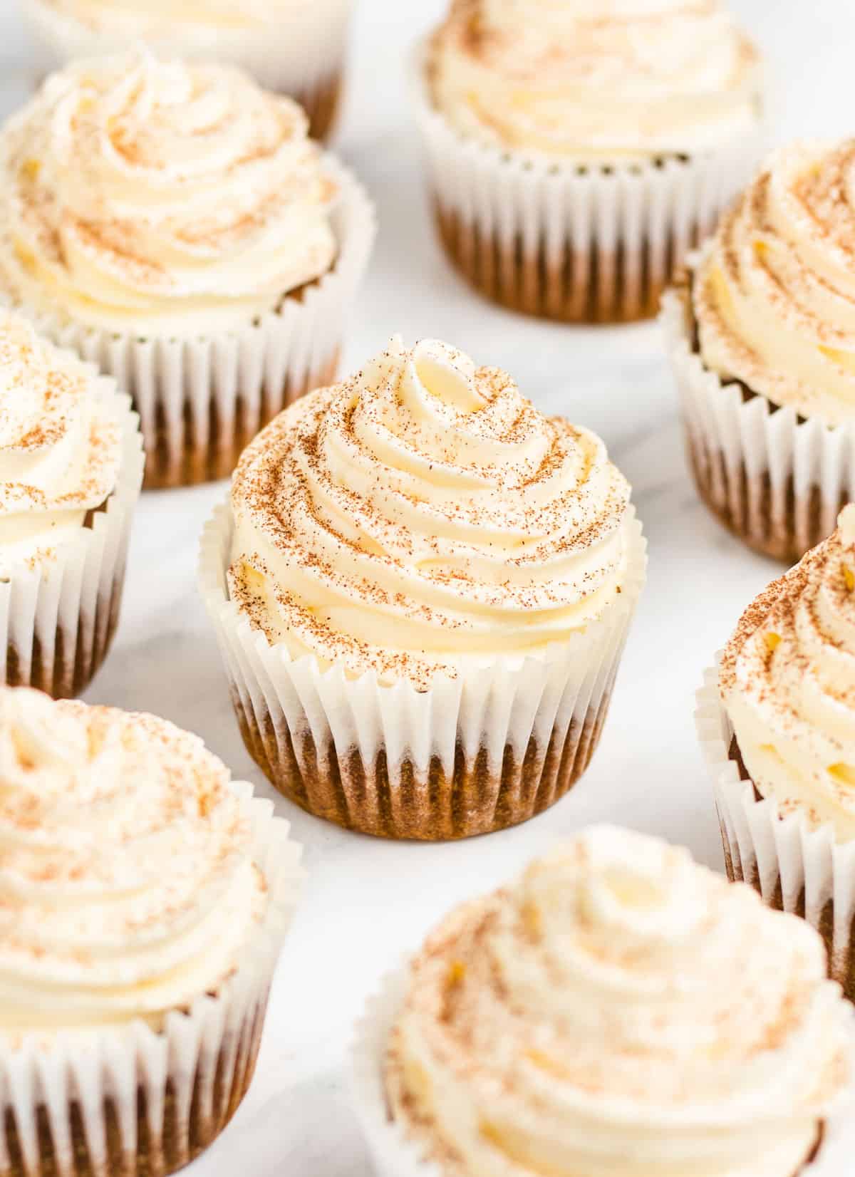 A bunch of frosted pumpkin cupcakes on a white background.