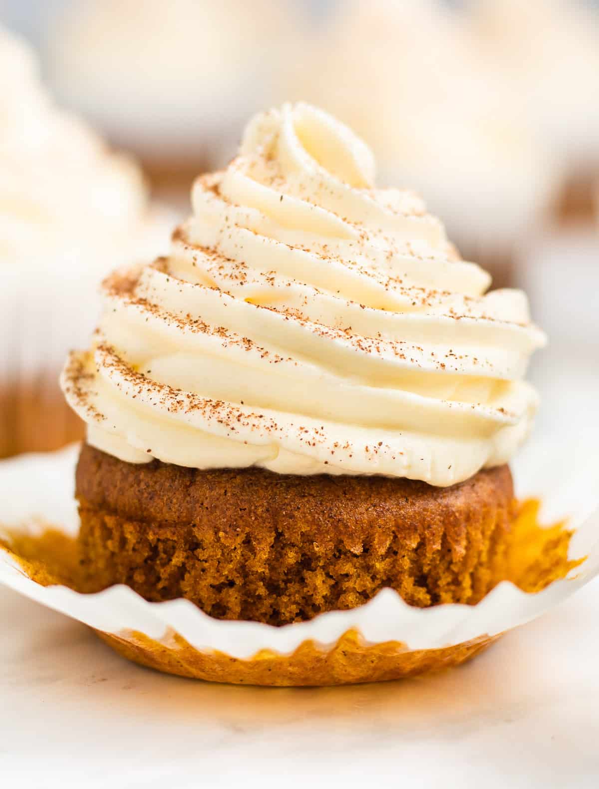 A single pumpkin cupcake close up with the liner peeled away.