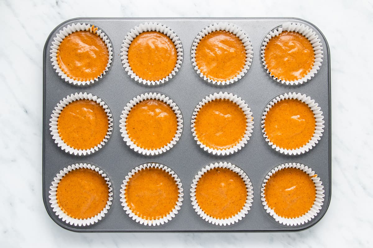 A cupcake pan filled with pumpkin cupcake batter.
