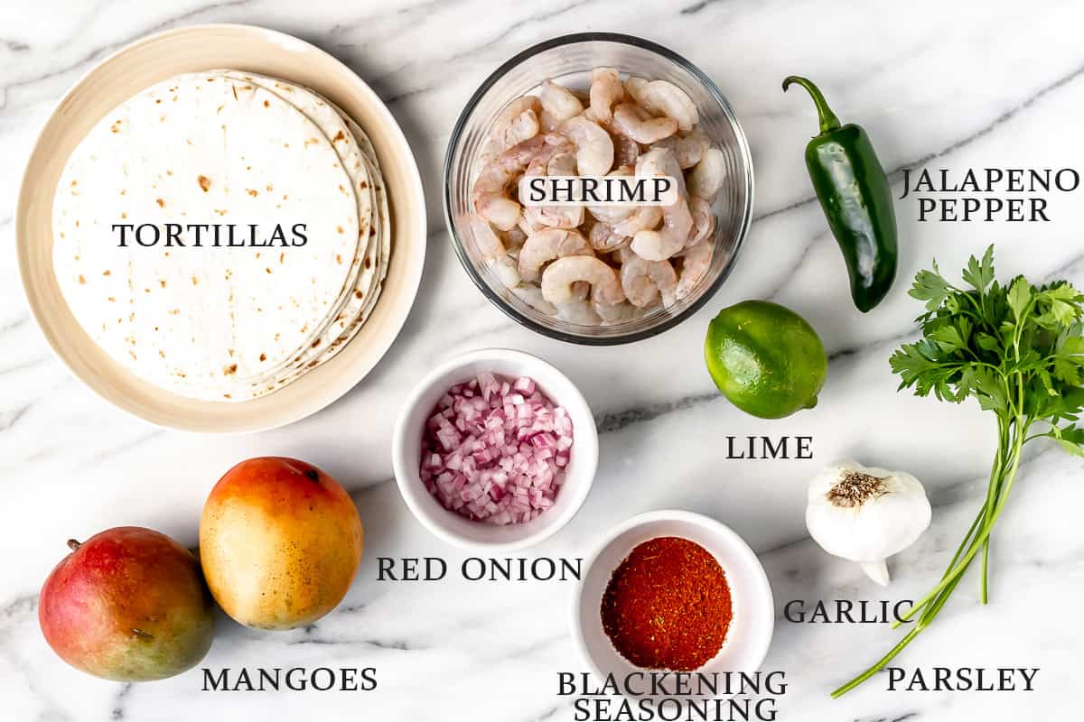 Ingredients for blackened shrimp tacos on a marble background with text overlay.