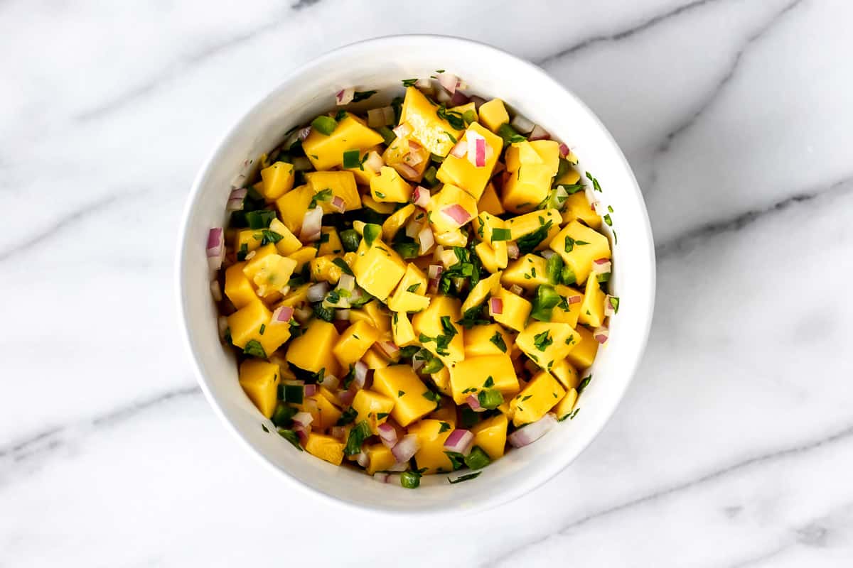 Mango salsa in a white bowl on a marble background.