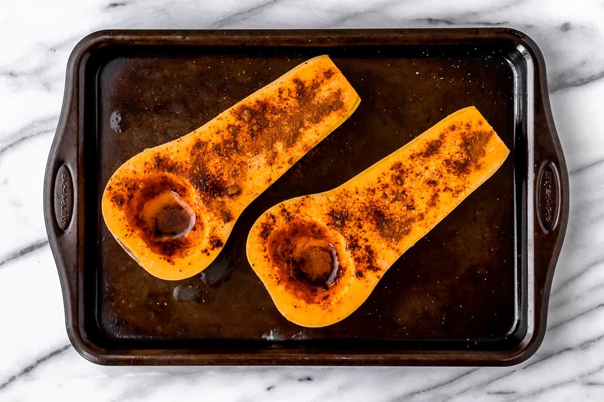 Butternut squash halves with butter and cinnamon on them on a baking sheet.