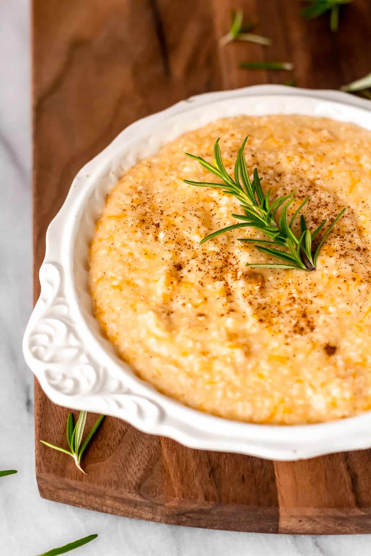 Close up of butternut squash grits in a white bowl on a wood background.