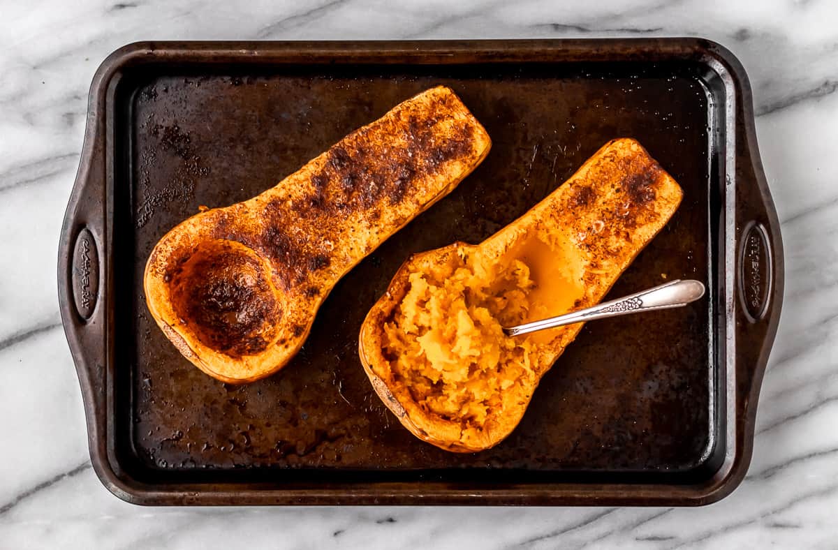 Roasted butternut squash halves with one scrapped out with a spoon.
